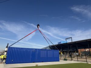 Blue 40 ft commercial shipping container being set by crane at ONT Field, home of the Ontario Tower Buzzers